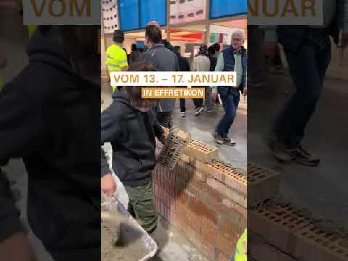 Ein Kind, das einen Kapuzenpulli und eine grüne Hose trägt, verteilt Mörtel auf Ziegelsteinen, während es in einem Haus eine Mauer baut. Im Hintergrund stehen mehrere Personen und schauen zu. Der überlagerte Text lautet: VOM 13. - 17. JANUAR IN EFFRETIKON.