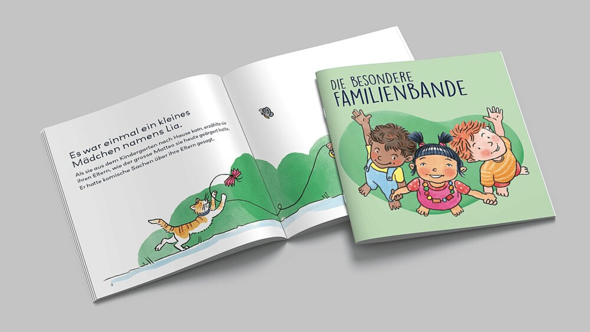 Gezeigt wird ein deutsches Kinderbuch mit dem Titel Die besondere Familienbande, auf dessen illustriertem Einband vier lächelnde Kinder zusammensitzen. Die aufgeschlagene Seite zeigt eine Katze, die einen Schmetterling jagt, und einen Text, der eine Geschichte über ein Mädchen namens Lia erzählt.