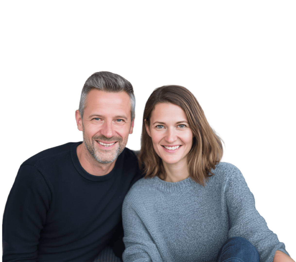 Ein Mann und eine Frau sitzen dicht beieinander und lächeln beide in die Kamera. Der Hintergrund ist schlicht weiß, und die beiden wirken entspannt und glücklich; sie tragen legere Pullover.