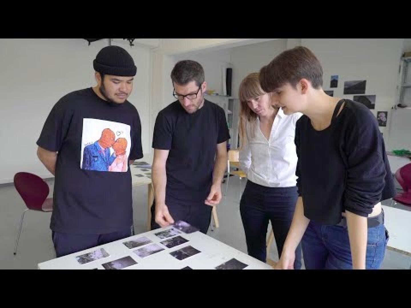 Vier Personen stehen um einen Tisch herum und betrachten mehrere Fotos, die vor ihnen ausgebreitet sind. Sie scheinen die Bilder in einem gut beleuchteten, modernen Raum zu diskutieren oder zu analysieren.