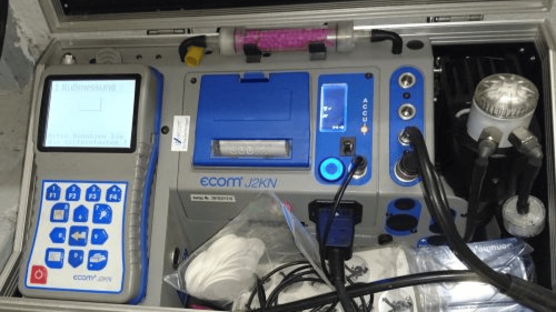 Nahaufnahme eines geöffneten tragbaren Gasanalysator-Kits mit einem Steuergerät mit blauen Tasten, einem Bildschirm, Kabeln, Schläuchen und verschiedenen Zubehörteilen, die ordentlich im Inneren des Koffers angeordnet sind.