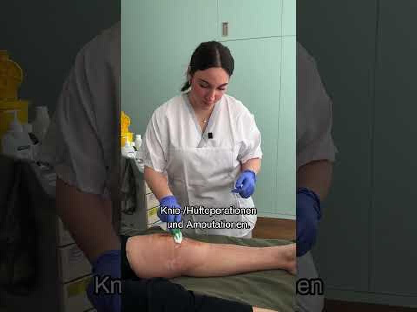 Ein Krankenpfleger in weißem Kittel und blauen Handschuhen behandelt die Beinwunde eines Patienten in einer Klinik. Auf dem Bild sind deutsche Untertitel zu sehen.