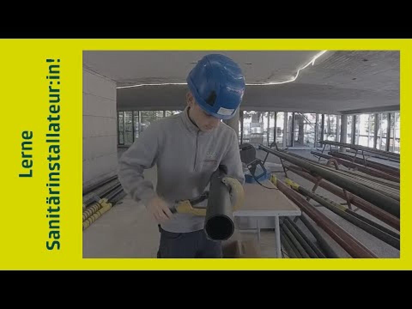 Eine Person mit einem blauen Schutzhelm arbeitet auf einer Baustelle an einem schwarzen Rohr. Links ist auf gelbem Hintergrund der Text „Lerne Sanitärinstallateurin!“ zu lesen.