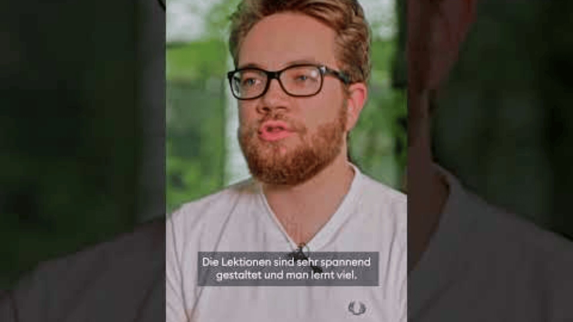 Es spricht ein bärtiger Mann mit Brille, der ein helles Hemd trägt. Der Hintergrund ist unscharf und grün. Der deutsche Text auf dem Bild lautet: Die Lektionen sind sehr spannend gestaltet und man lernt viel.