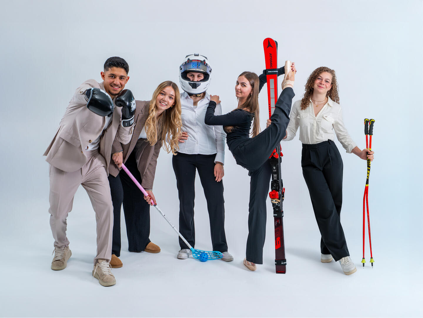 Fünf Personen in Business-Kleidung posieren spielerisch mit Sportausrüstung – Boxhandschuhe, ein Hockeyschläger, ein Motorradhelm, eine Tanzpose mit Skiern und Skistöcke – vor einem schlichten weißen Hintergrund.