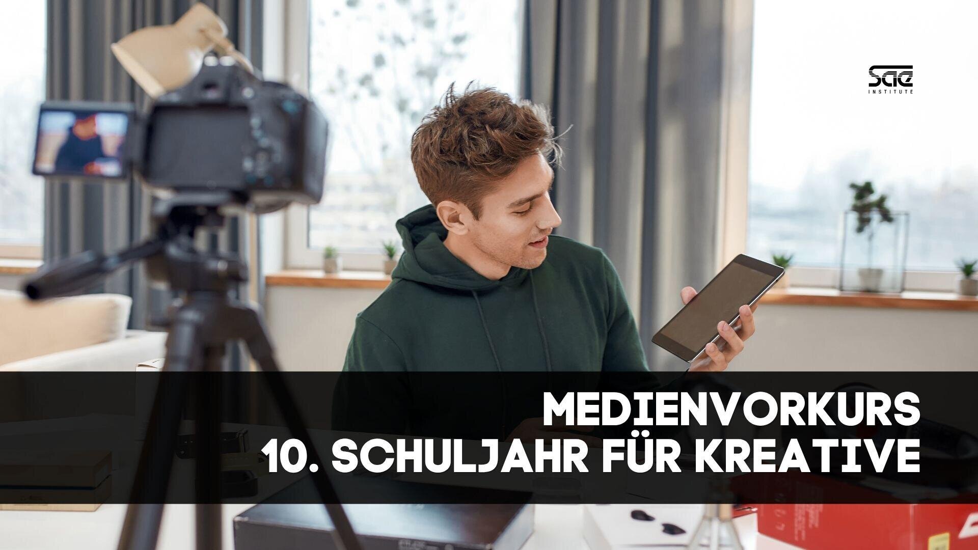 Ein junger Mann in einem grünen Kapuzenpulli hält ein Tablet in der Hand und spricht in eine Kamera auf einem Stativ. Textüberlagerung lautet: MEDIENVORKURS 10. SCHULJAHR FÜR KREATIVE. Die Szene deutet auf einen kreativen Medienkurs oder Workshop hin.